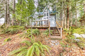 A cabin surrounded by dense forest, with a wooden staircase leading to a deck. - Riverfront home close to skiing & fishing with beach access & huge VHS library (Rhododendron)