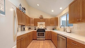 A kitchen with wooden cabinets, a stainless steel stove, a dishwasher, and a window providing natural light. - Modern Beach House with Partial Ocean Views - Walk to Nye Beach & Attractions (Newport)