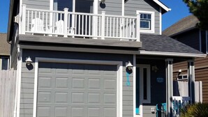 A two-story house with a white garage door, a balcony with white railings, and a porch with a mailbox. - Modern Beach House with Partial Ocean Views - Walk to Nye Beach & Attractions (Newport)