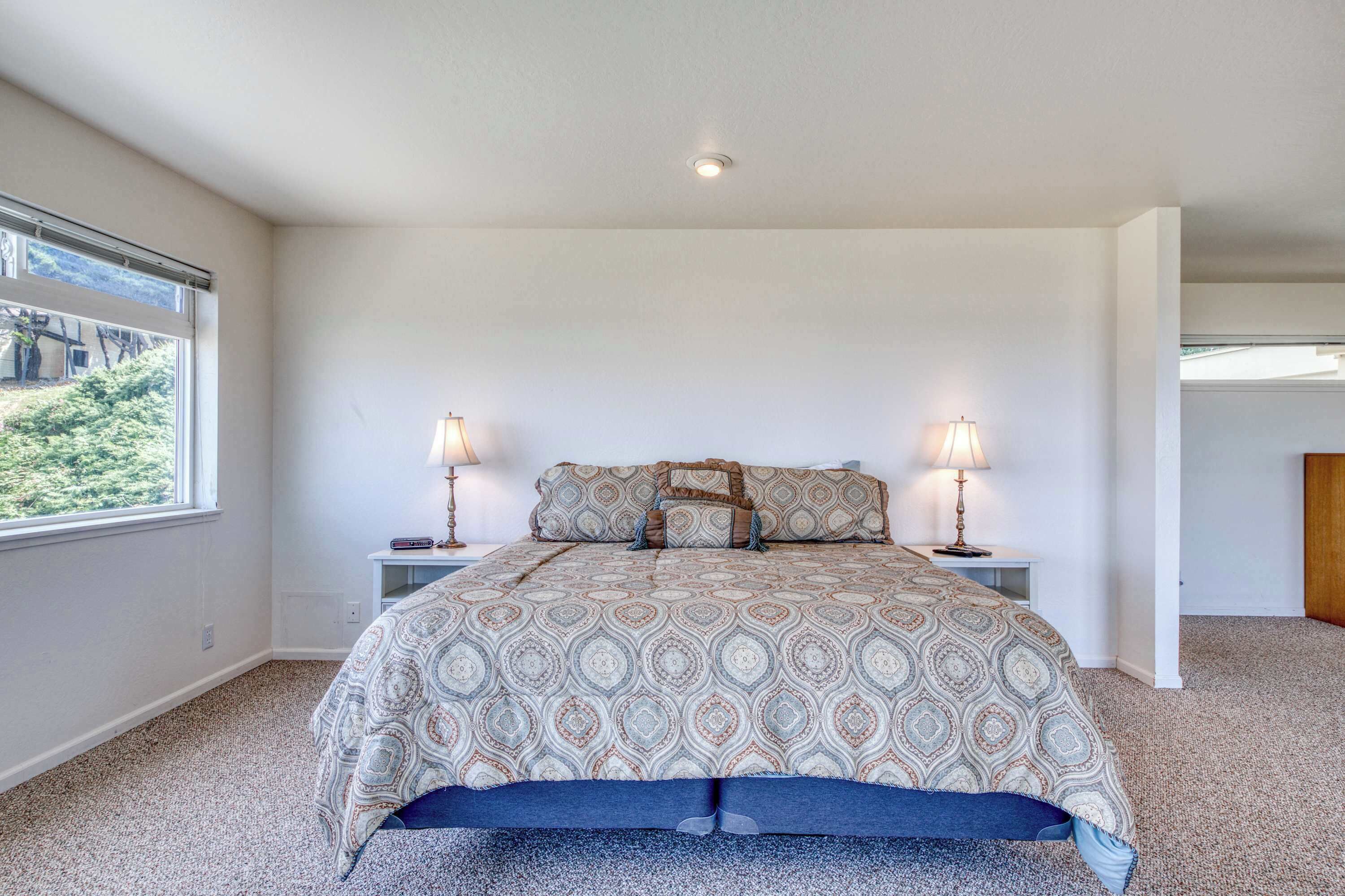 A bedroom with a large bed, two bedside tables, a window, and a view of greenery outside.
