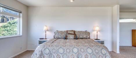 A bedroom with a large bed, two bedside tables, a window, and a view of greenery outside.