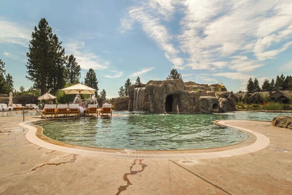 A pool area with lounge chairs, a waterfall feature, and a rocky landscape. - Luxury home with private hot tub, bikes & fireplace - quarry pool & tennis access (Sunriver)
