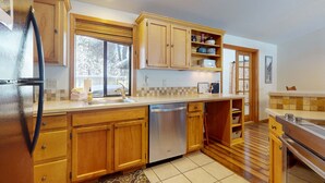 A kitchen with wooden cabinets, a dishwasher, and a window. - Comfy Home with Private Hot Tub, SHARC Passes & Entertainment (Sunriver)