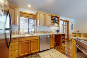 A kitchen with wooden cabinets, a dishwasher, and a window. - Comfy Home with Private Hot Tub, SHARC Passes & Entertainment (Sunriver)