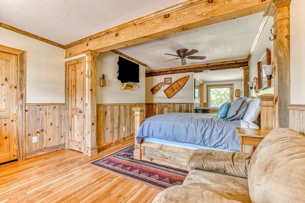 A wooden-paneled bedroom with a bed, a ceiling fan, and a large mirror.