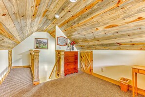 A room with a sloped ceiling, wooden beams, a dresser, a mirror, and a picture on the wall.