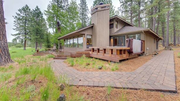 Une maison moderne dotée d’une grande terrasse, d’une cheminée et offrant une vue sur la forêt environnante.