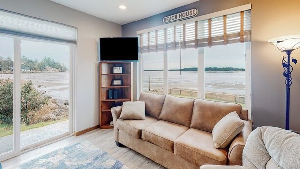 Una sala de estar con sofá, estantería, televisor de pantalla plana y un amplio ventanal con vista a la playa.