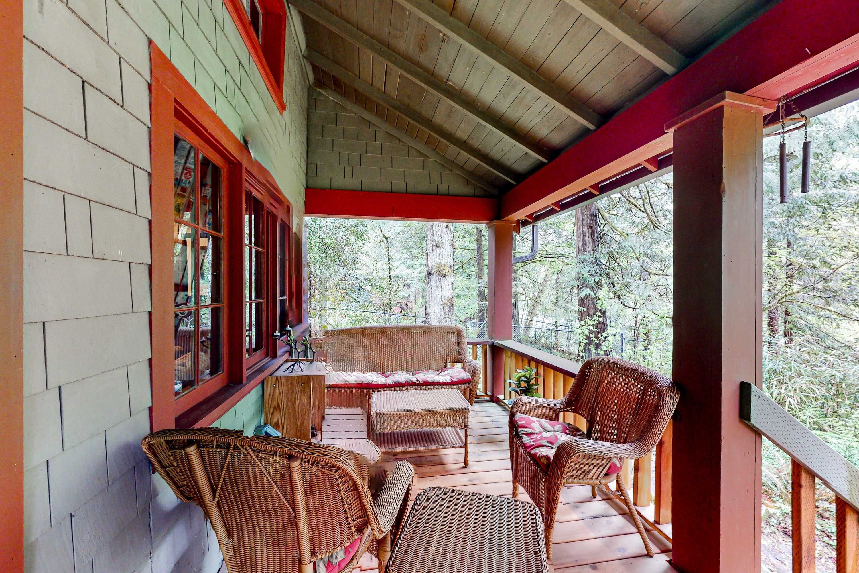 Een overdekte veranda met rieten meubels, een bakstenen muur en uitzicht op het bos.