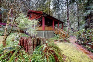 A cabin with a wooden deck, surrounded by dense forest. - Unwind in nature's embrace at a 1925 cabin with hot tub & river views (Sandy)