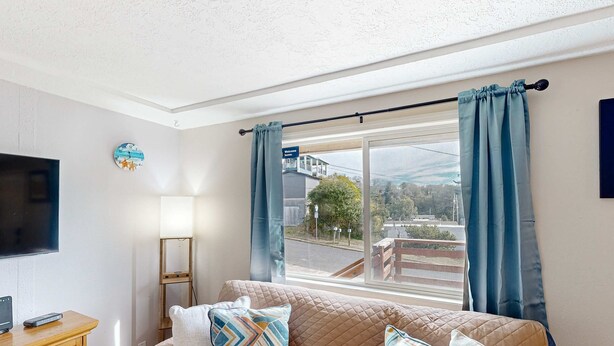 Ein Wohnzimmer mit einer Couch, Kissen, einem Fernseher, einer Lampe und einem Fenster mit Vorhängen.