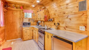 Ein Interieur einer Holzhütte mit einer Küche, die Holzschränke, einen Herd, eine Mikrowelle und ein Waschbecken zeigt.