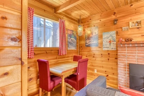 A wooden cabin interior with a dining table, red upholstered chairs, a fireplace, and wall decorations including a poster of the Olympic rings and a mountain scene. - Rustic & cozy cabin with fast WiFi & games - close to slopes, dining & golf (Government Camp)