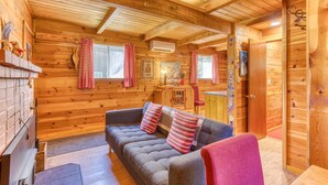 Ein Blockhaus-Interieur mit einer Couch, roten und weißen karierten Vorhängen, einem Kamin und einer Holzbalkendecke.