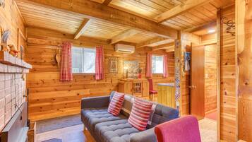 L’intérieur d’une cabane en rondins, avec un canapé, des rideaux à carreaux rouges et blancs, une cheminée et un plafond en bois.