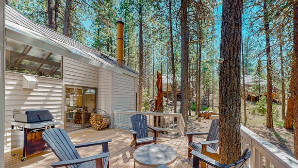 Une terrasse en bois, dotée de mobilier d’extérieur, d’un barbecue et offrant une vue sur la forêt environnante.
