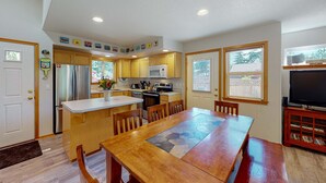 A kitchen with a central island, wooden cabinets, a refrigerator, microwave, and a dining area with a table and chairs. - Dog-friendly 2-story duplex with gas fireplace, enclosed yard, gas grill & W/D (Manzanita)