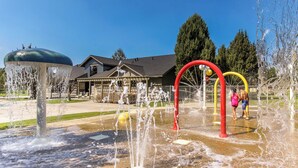 Ein Wasserspielplatz mit mehreren Sprudlern und einem Haus im Hintergrund.