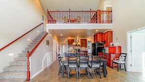 A spacious dining area with a high ceiling, a staircase with a red railing, and a kitchen with red cabinets. - Dog-friendly ocean view home with WiFi, remote work spaces, and washer&dryer (Gold Beach)