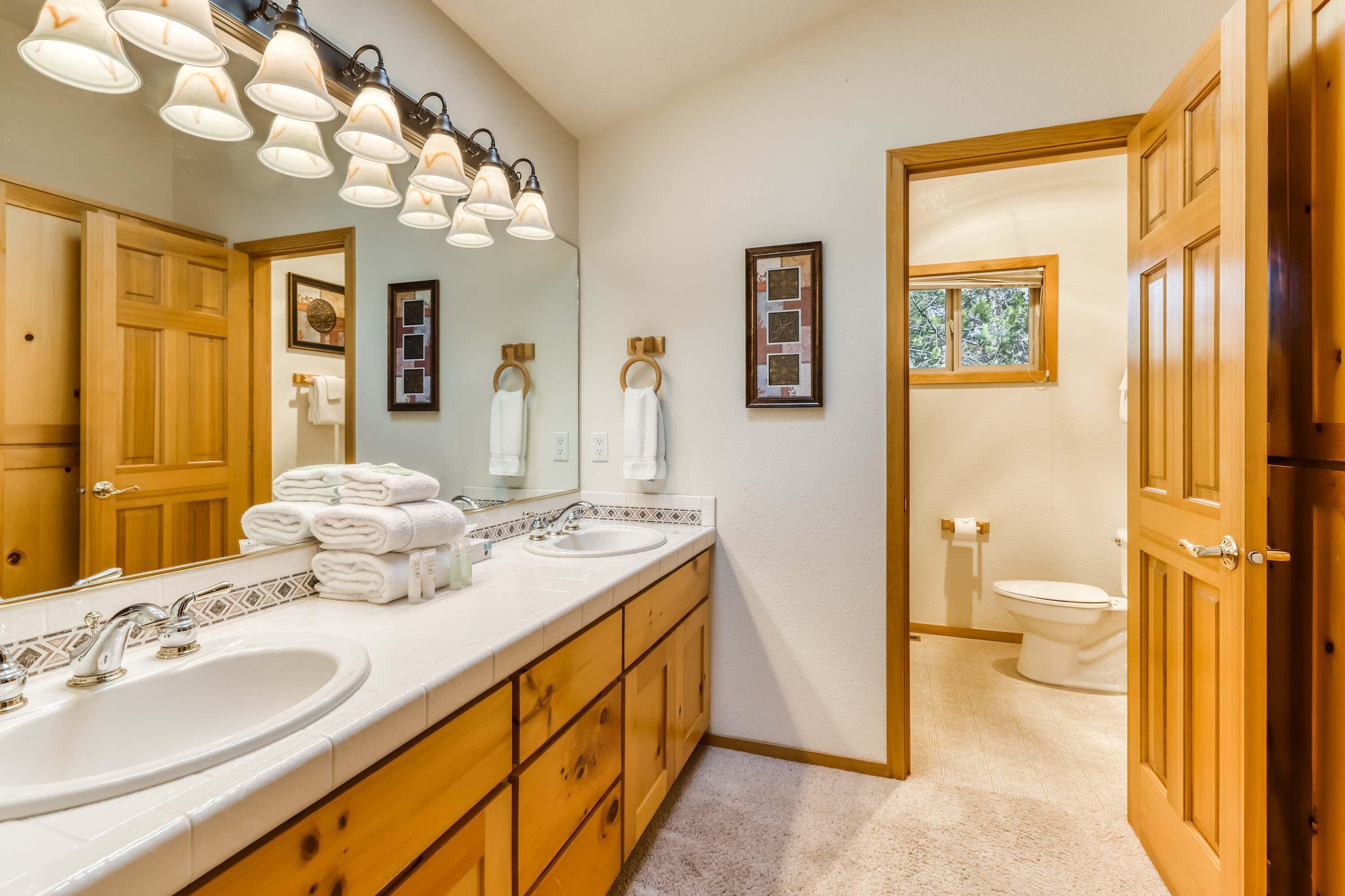 A bathroom with a large mirror, two sinks, wooden cabinets, and a toilet.