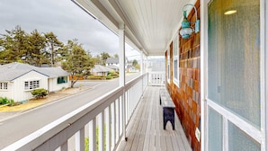 A covered porch with a wooden railing, a bench, and a view of a street with houses. - Beautiful Cape Cod cottage - one block from the beach with covered balcony & W/D (Seaside)