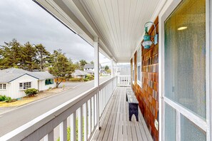 A covered porch with a wooden railing, a bench, and a view of a street with houses. - Beautiful Cape Cod cottage - one block from the beach with covered balcony & W/D (Seaside)