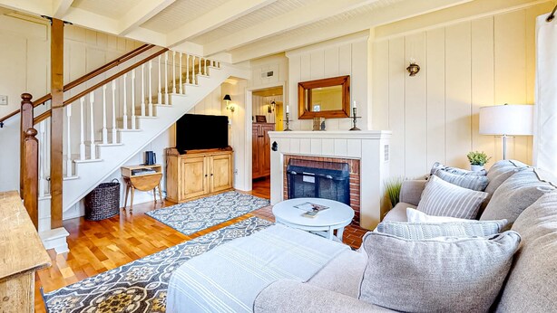 A spacious living room with a staircase, a fireplace, and a cozy seating area. - Beautiful Cape Cod cottage - one block from the beach with covered balcony & W/D (Seaside)