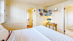 A bedroom with a bed, a bedside table with a lamp, and a bookshelf. - Beautiful Cape Cod cottage - one block from the beach with covered balcony & W/D (Seaside)