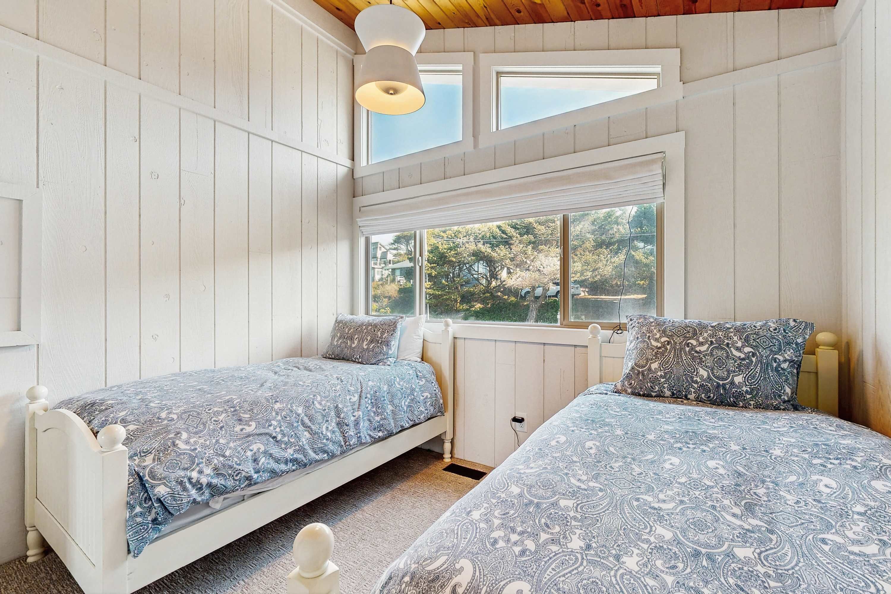 A bedroom with two single beds, a window with a view, and a ceiling light fixture.