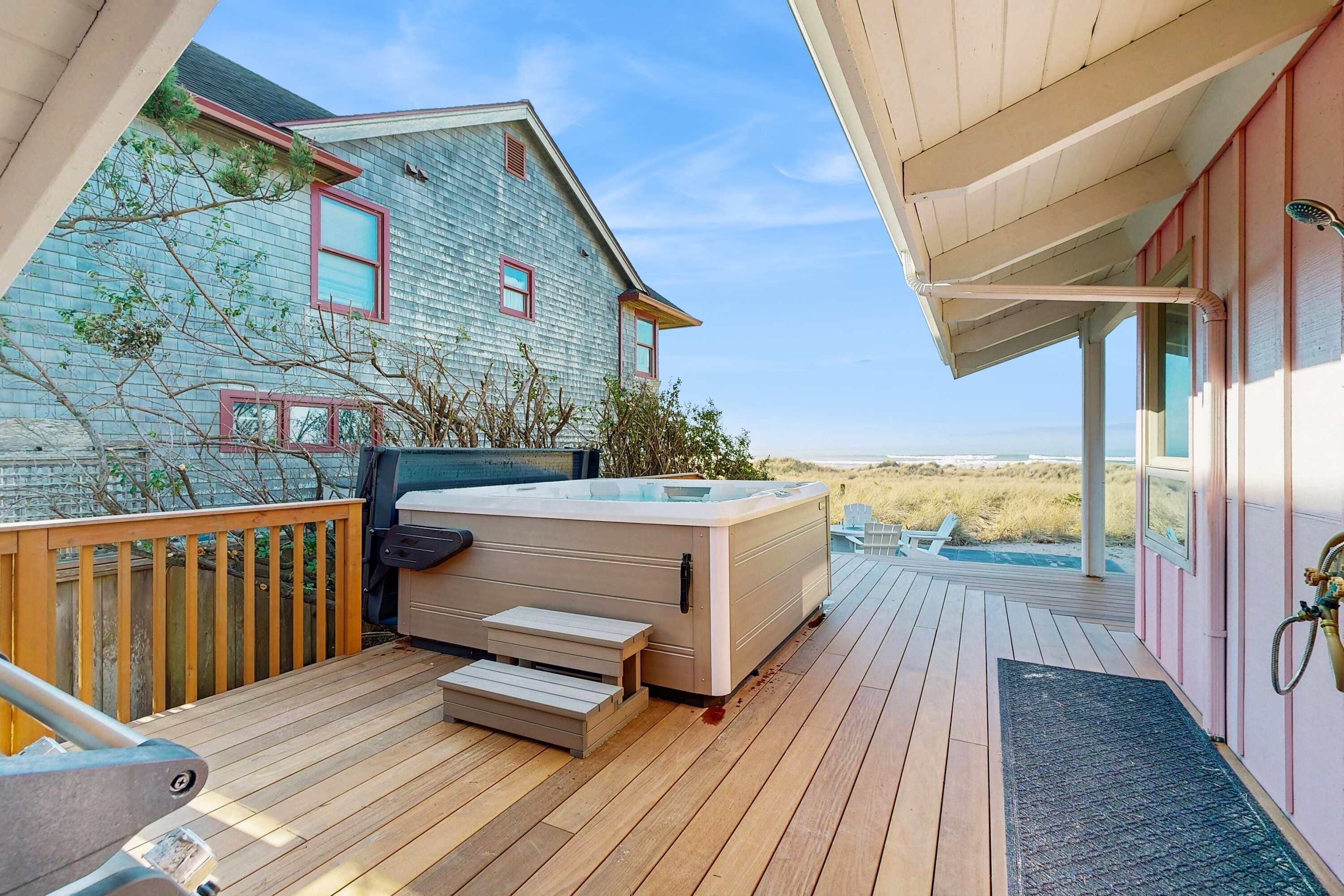 A hot tub on a wooden deck with a view of a house and beach.