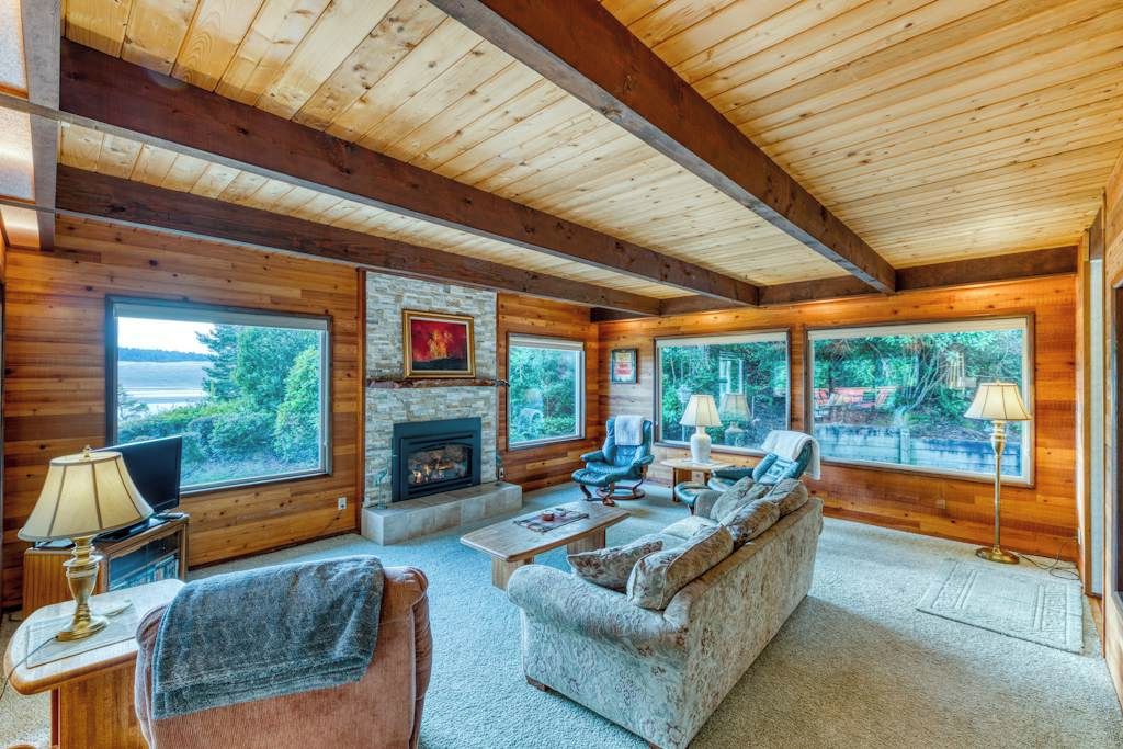 A log cabin interior with a fireplace, large windows, a sofa, and a television.