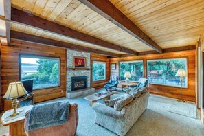 A log cabin interior with a fireplace, large windows, a sofa, and a television. - Gorgeous riverfront house with entertainment - near Bay Street and the beach (Florence)