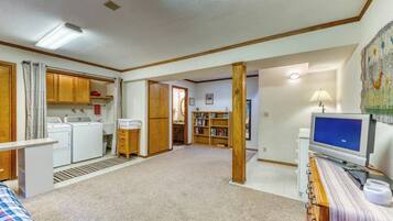 A spacious living area with a television, a bookshelf, and a kitchen area with appliances.