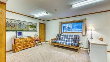 A room with a wooden dresser, a plaid sofa, a television on a stand, a window with curtains, and a lamp.