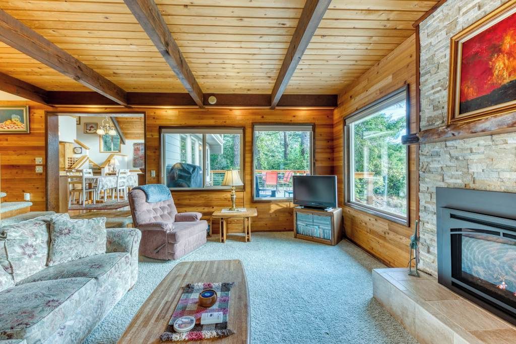A cozy cabin interior with a fireplace, wooden walls, a television, and a dining area.