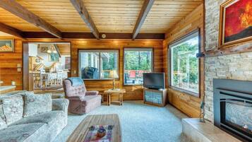 A cozy cabin interior with a fireplace, wooden walls, a television, and a dining area.