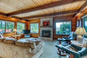 A log cabin interior with a fireplace, large windows, a sofa, and a television. - Gorgeous riverfront house with entertainment - near Bay Street and the beach (Florence)