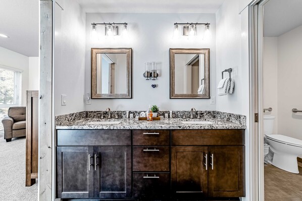 Un baño con tocador doble, dos espejos, lavabo e inodoro.
