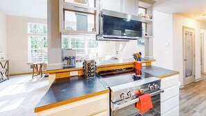 Une cuisine équipée d’une cuisinière, d’un four et d’un four à micro-ondes. On y trouve des placards au-dessus du plan de travail et une fenêtre avec des stores.