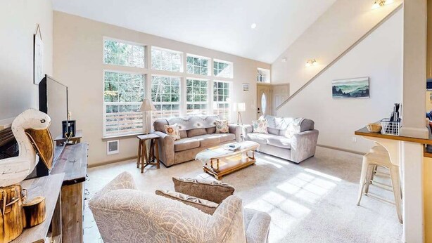 Un salon spacieux avec un haut plafond, de grandes fenêtres, une cheminée et un coin salon confortable.