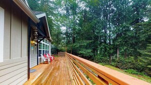 Une terrasse en bois avec une balustrade, un bâtiment doté d’un porche et, au fond, une zone boisée.