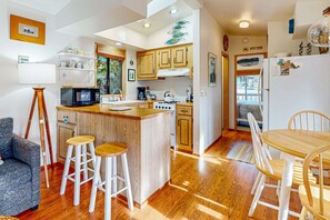 Una cocina compacta con armarios de madera, una isla central con taburetes, una mesa de comedor con sillas y un refrigerador.