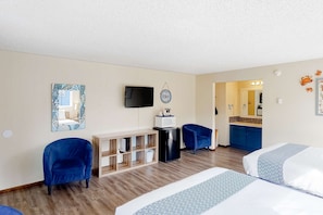 Une chambre d’hôtel avec deux lits, une télévision, un bureau avec un micro-ondes, une chaise et une petite kitchenette.