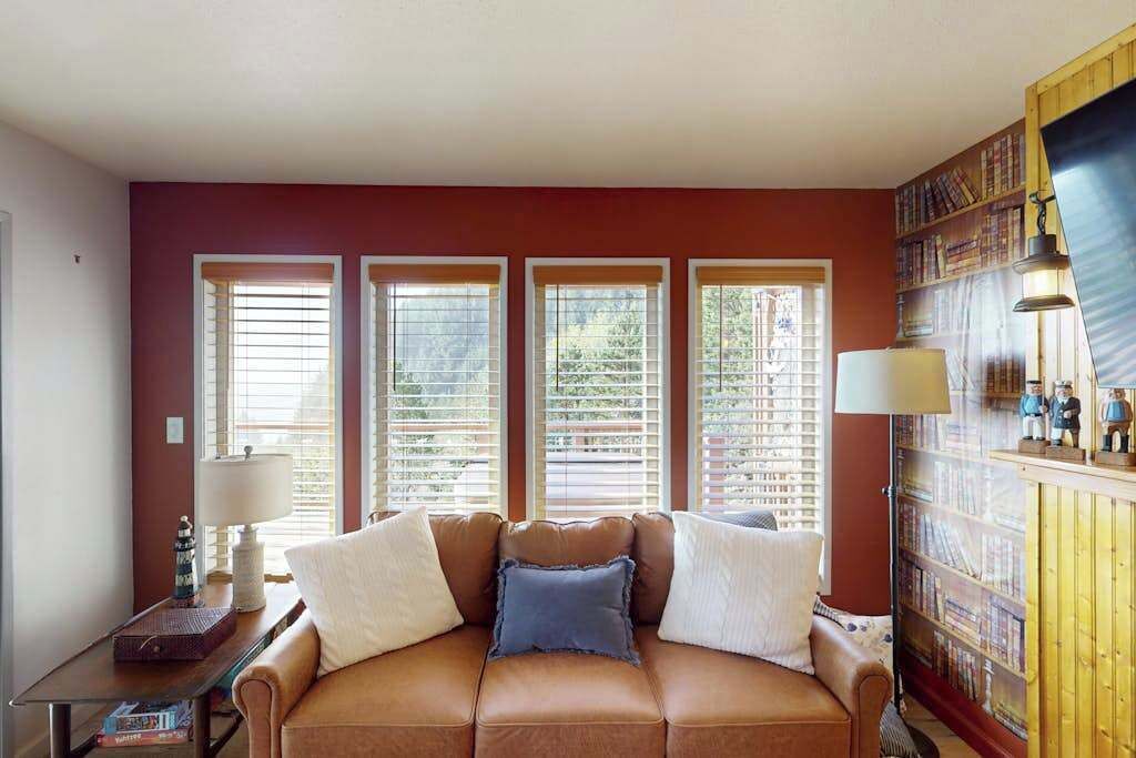 A room with a brown leather sofa, a side table with a lamp, and a bookshelf.