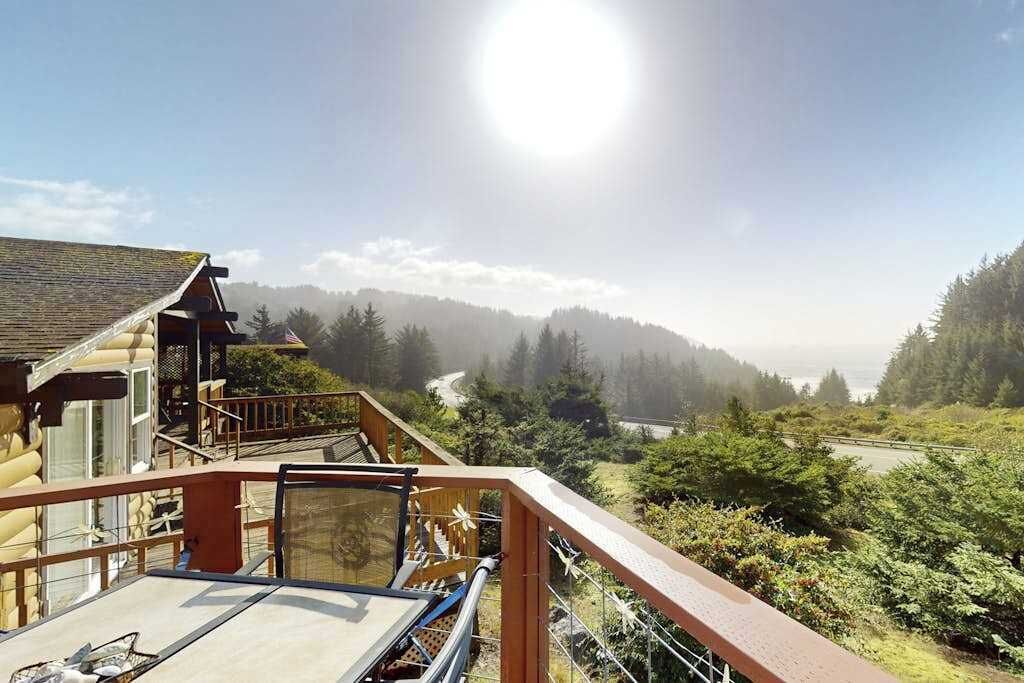 A wooden cabin with a balcony overlooking a forested valley and a river.