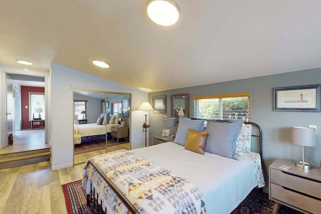 A bedroom with a bed, bedside tables, a mirror, and a window with a view.