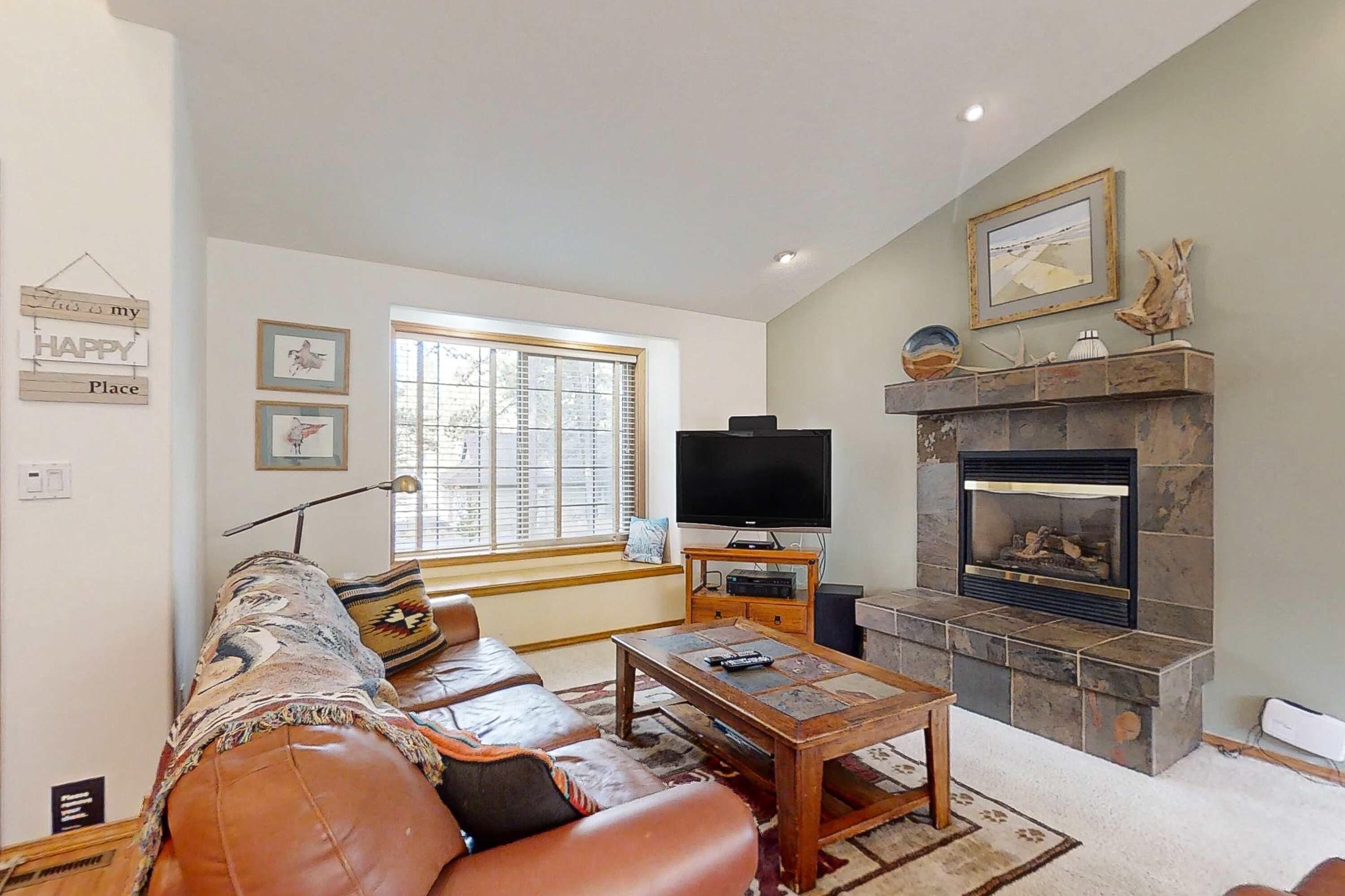 A living room with a sofa, a television, a fireplace, and a window with blinds.
