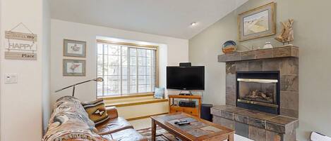 A living room with a sofa, a television, a fireplace, and a window with blinds.