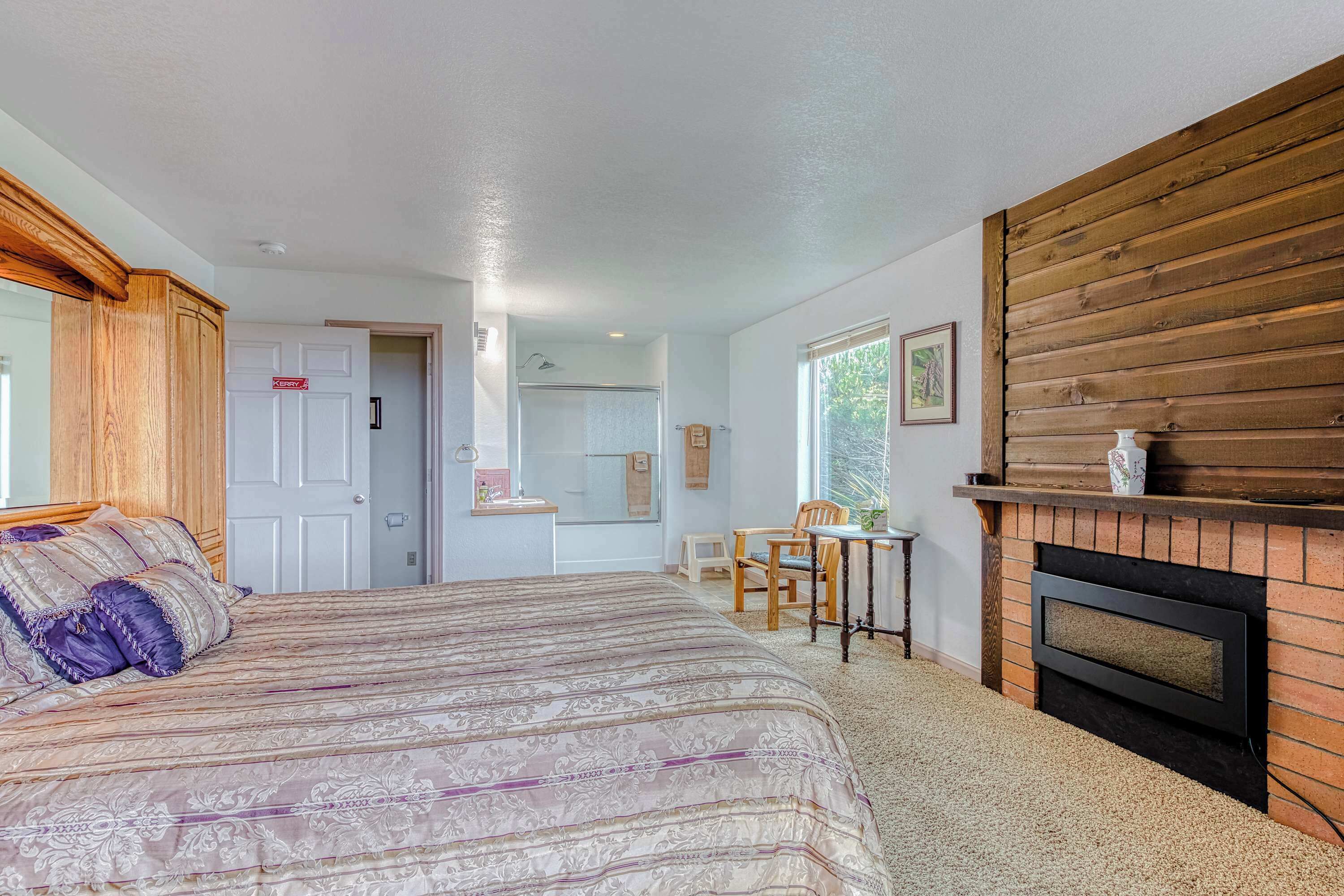 A bedroom with a bed, a fireplace, a window, and a door leading to a bathroom.