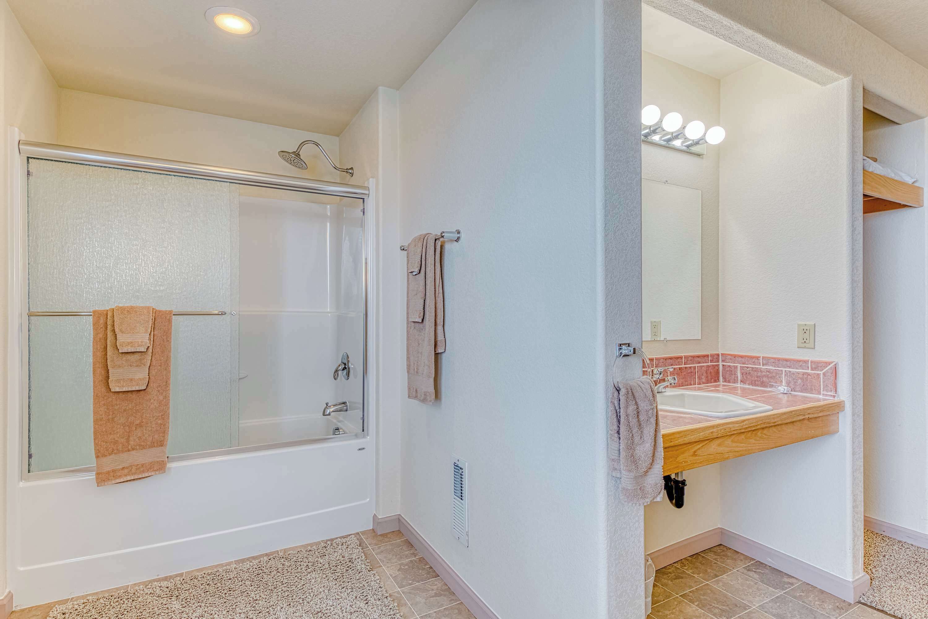 A bathroom with a glass-enclosed shower, a sink with a vanity, and a mirror with lights.
